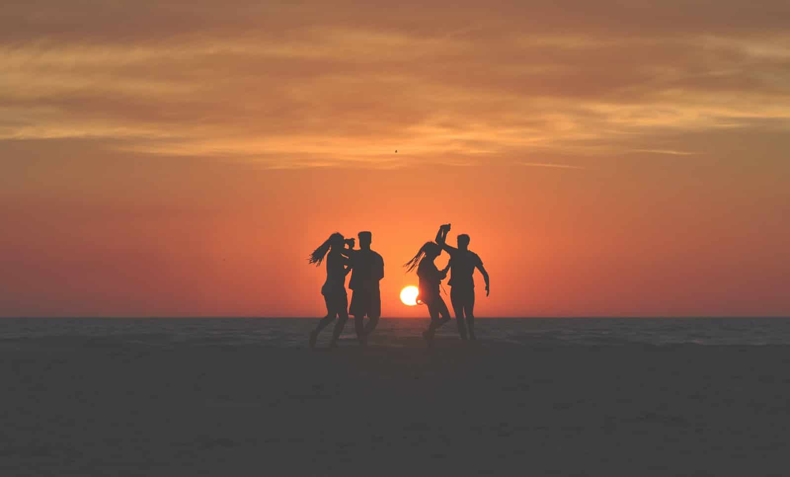 photo de silhouette de quatre personnes dansant sur le sable près du rivage